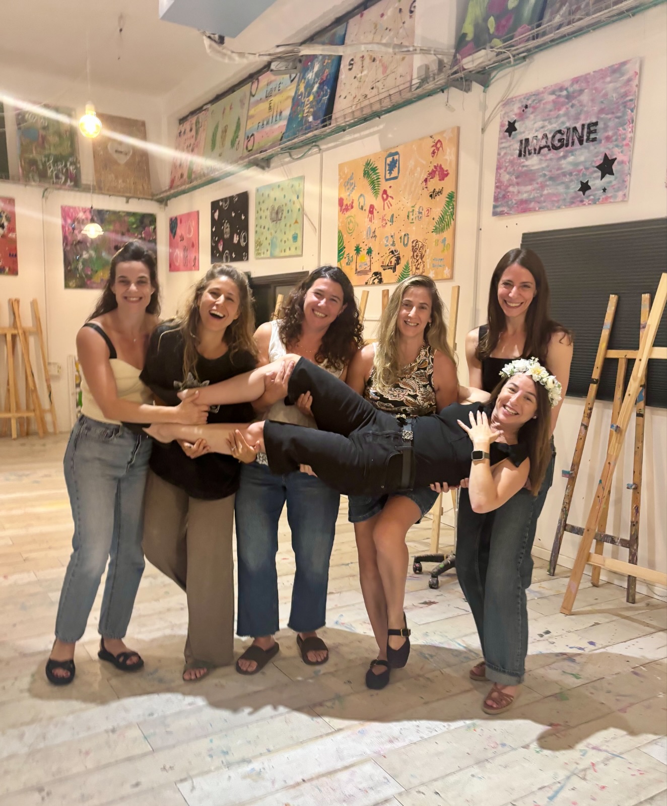 קבוצת חברות מחייכות בסטודיו, מרימות את חברתן עם זר פרחים